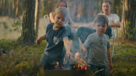 Two-boys-sitting-by-a-fire-against-a-tent-in-the-woods-on-the-shore-of-the-lake-fry-marshmallows-on-fire.-Brothers-3-6-years-together-burn-sticks-on-fire